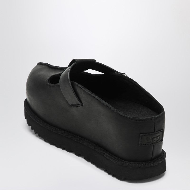 Black Ugg clogs with a round toe, Velcro strap closure, and logo lettering on the strap. The clogs have a flat rubber sole.
