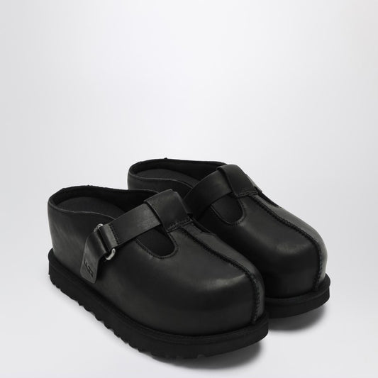 A pair of black UGG clogs with a round toe, Velcro strap closure, and logo lettering on the strap.
