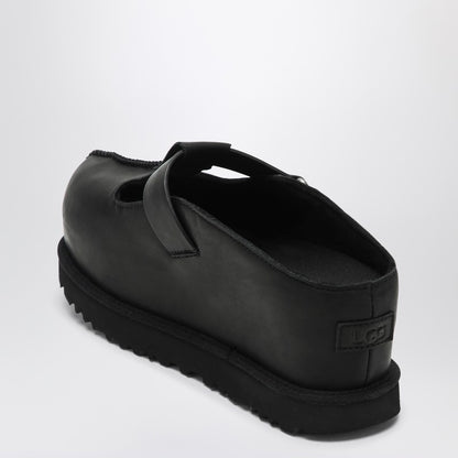 Black Ugg clogs with a round toe, Velcro strap closure, and logo lettering on the strap. The clogs have a flat rubber sole.